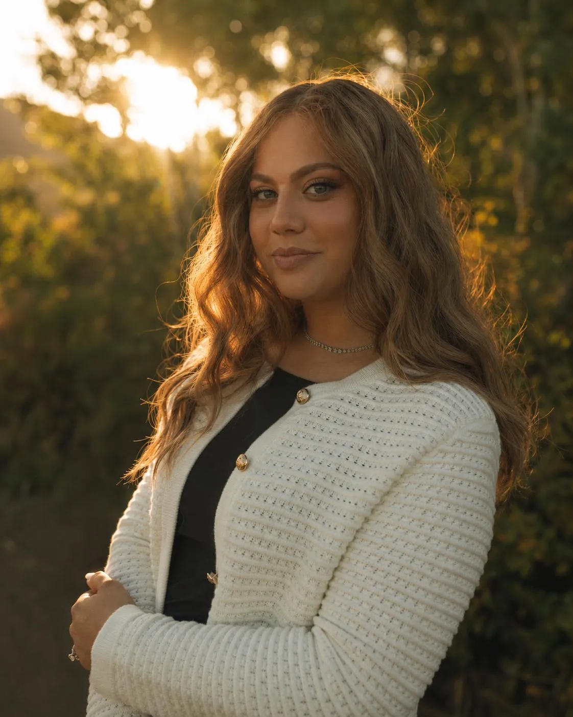 Aliza Jacobs in a cream cardigan at golden hour, arms gently folded, looking warmly toward the camera.