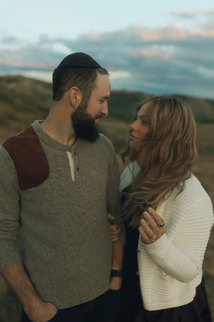 Aliza and Rabbi Meir Jacobs standing close together at dusk, gazing into each other's eyes, hills behind them.